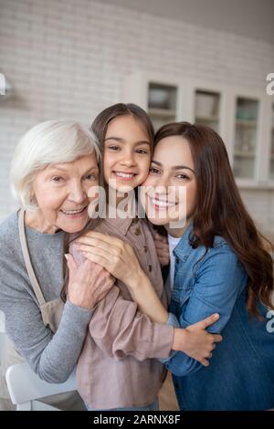 Drei glückliche Frauen umarmen sich in der Küche. Stockfoto