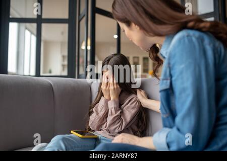 Weinende Tochter und tröstende Mutter, die auf der Couch sitzt. Stockfoto