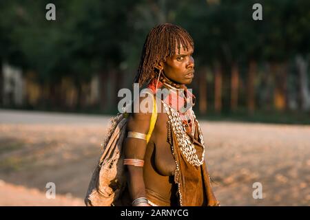 Hamer Woman, die die Straße im Dorf Dimeka, Omo Flusstal, Äthiopien überquert. Stockfoto