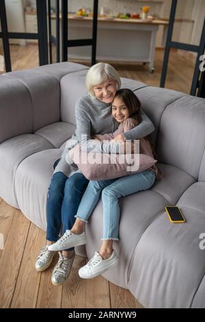Großmutter und Enkelin sitzen umarmend auf einem Sofa. Stockfoto