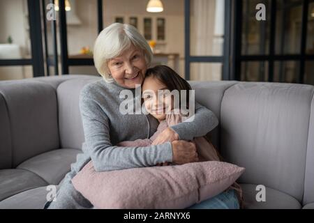 Großmutter und Enkelin umarmen und lächeln auf einem Sofa sitzen. Stockfoto