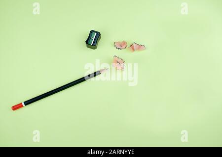 Ein dunkelschwarzer Bleistift mit roter Spitze neben einem schwarzen Bleistiftschärfer und einigen Bleistiftspänen Stockfoto