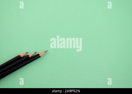 Drei dunkelschwarze, geschärfte Holzbleistifte werden über einem hellgrünen Papierhintergrund platziert, wo sie alle in die gleiche Richtung nach oben zeigen Stockfoto