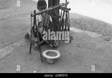 Aufnahmen von Bildern in der Indian Life Street. Kleiner (behinderter?) Junge als Straßenmusiker spielt auf einer Angklung. Für ihn ein Hut für Change Annotation: DJK Datum: 24. August 1948 Ort: Indonesien, Niederländische Ostindien Stockfoto