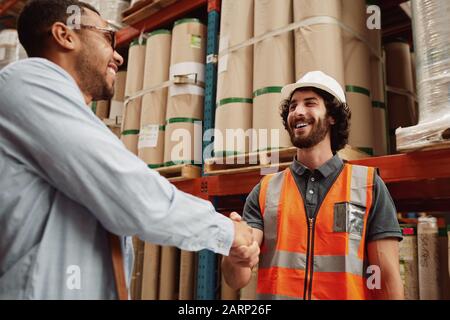 Junge Partner beglückwünschen sich gegenseitig zu einem neuen Geschäftsabschluss, während sie in einer modernen Fabrik stehen Stockfoto