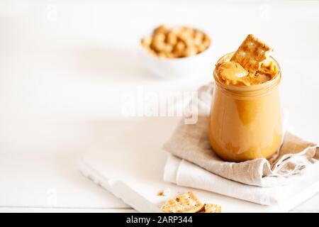 Hausgemachte natürliche Peannussnuss Cashew cremige Butter in Glasbecher und Löffel auf weißem Hintergrund.Kopierraum, horizontale Ausrichtung Stockfoto
