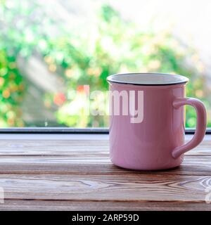 Eine pinkfarbene Tasse Tee steht auf einem Holzfensterschweller vor dem Hintergrund eines Sommergartens Stockfoto