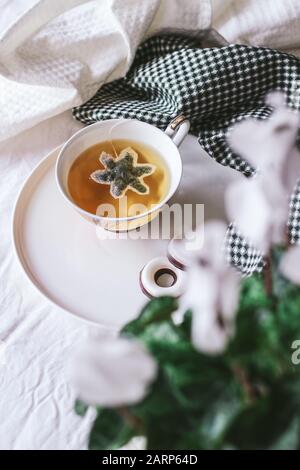 Teetasse mit Schneeflocken-Teetasche auf weißem Grund und weiße Cyclamenblüte im ersten Plan in Bokeh (verschwommen) Stockfoto