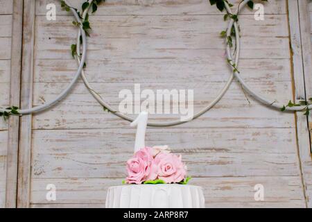 Oberteil mit luxuriösem Kuchen mit Rosen und einer einjährigen weißen Kerze auf hellem Holzhintergrund. Celebration Concept. Stockfoto