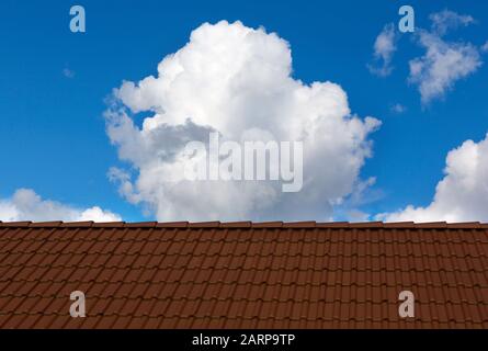 Dachhaus mit blauem Himmel und Wolken. Dachziegel und Himmel am sonnigen Tag. Stockfoto