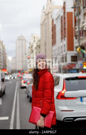 Lächelnde junge Frau in rotem Mantel und ein Laptop, der in die Innenstadt läuft Stockfoto