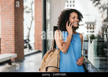 Lächelnde junge Frau, die beim Einkaufen auf ihrem Handy spricht Stockfoto