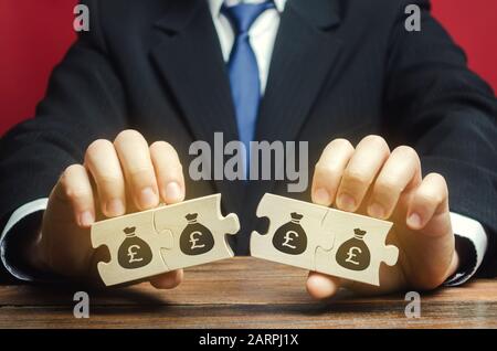 Geschäftsmann trennt die Holzpuzzle mit einem Bild von Geld. Das Konzept des Finanzmanagements und der Verteilung der Mittel. Sparen und Investieren. Stockfoto