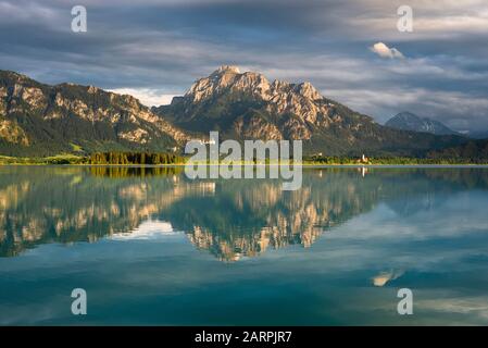 Schloss Neuschwanstein, Schloss Hohenschwangau und die bayerischen Alpen bei Sonnenuntergang spiegeln sich im Forggensee in Bayern wider Stockfoto