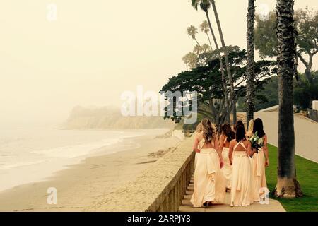 Eine Gruppe von Brautjungfern spazieren am Strand in Beverly Hills, Kalifornien. Weißer Sandstrand und nebeliges Wetter. Dame hält Blumenstrauß. Zu Fuß erreichbar. Stockfoto