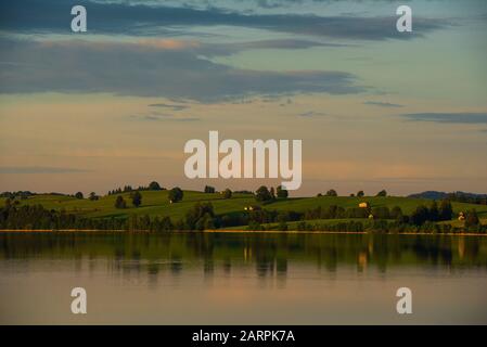 Blick über den Forggensee auf Wiesen, Weiden und Berge im letzten Sonnenlicht bei Sonnenuntergang, Bayern, Deutschland Stockfoto