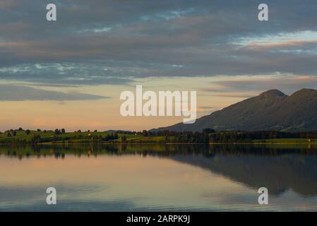 Blick über den Forggensee auf Wiesen, Weiden und Berge im letzten Sonnenlicht bei Sonnenuntergang, Bayern, Deutschland Stockfoto