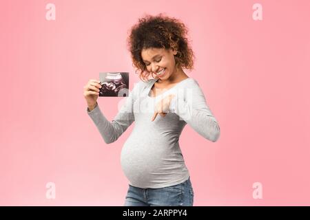 Sehen Sie hier! Angeregte afro-schwangere Frau mit Ultraschalluntersuchung Stockfoto