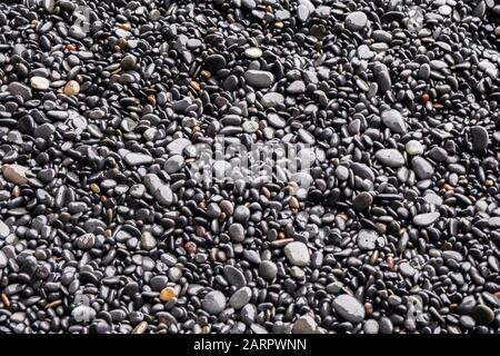 Hintergrund schwarzer Kiesel und Steine an den schwarzen Sandstränden von Reynisfjara in Island Stockfoto