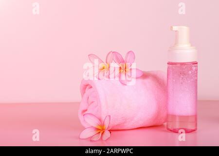 Spa-Zusammensetzung mit Handtuch, Blumen und Seifenflasche auf pinkfarbenem Hintergrund. Stockfoto