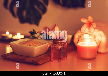 Spa-Zusammensetzung mit Schalen mit weißem und rosafarbenem Salz, Blumen, Handtuch und Kerzen und Blättern aus Monstera im Hintergrund Stockfoto