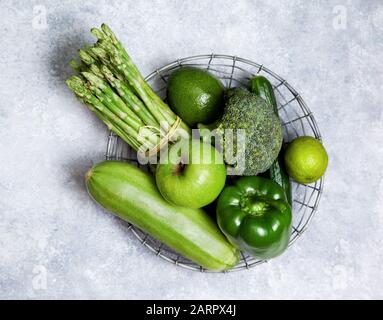 Frisches naturgrünes Gemüse und Obst in einem Metallkorb auf grauem Grund. Blick von oben Stockfoto