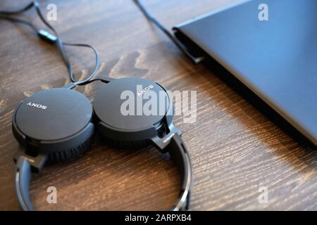 Sony Kopfhörer auf dem Bürotisch. Kopfhörer an Laptop angeschlossen, Speicherplatz kopieren. Musik bei der Arbeit hören - 2019.07.07 - Nischni Nowgorod, Russland Stockfoto