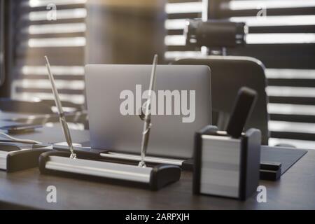 Moderner Büroarbeitsplatz. Business-Laptop am Arbeitsplatz für Chef, Chef oder andere Mitarbeiter. Notizbuch auf Arbeitstisch. Licht durch halb geöffnete Jalousien - 20 Stockfoto