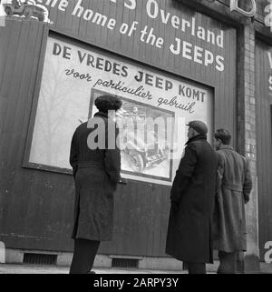Passanten sehen ein Plakat mit dem Text De Vredes Jeep Comes Date: 12. Dezember 1945 Schlagwörter: Plakate, Plakate Stockfoto