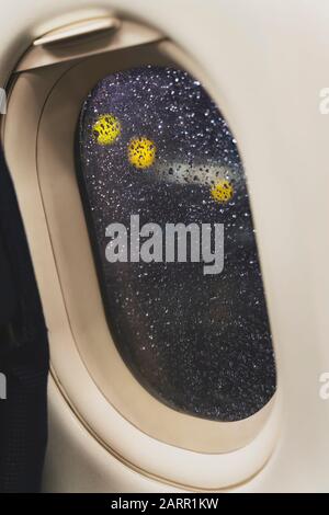 Nachtansicht von der Flugzeugbeleuchtung auf den Flughafenleuchten. Regenstreuung auf dem Porthole-Glas aufgrund von schlechtem Regenwetter. Flugzeug bringt Sie zu Stockfoto