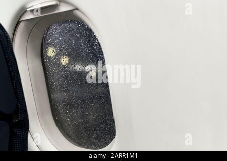 Nachtansicht von der Flugzeugbeleuchtung auf den Flughafenleuchten. Regenstreuung auf dem Porthole-Glas aufgrund von schlechtem Regenwetter. Flugzeug bringt Sie zu Stockfoto