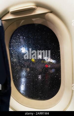 Nachtansicht vom Flugzeugsenkabinenfenster auf bunte Flughafenbeleuchtung. Wegen des schlechten Regenwitters ist die Regenstreuung im Sichtfeld. Flugzeug br Stockfoto
