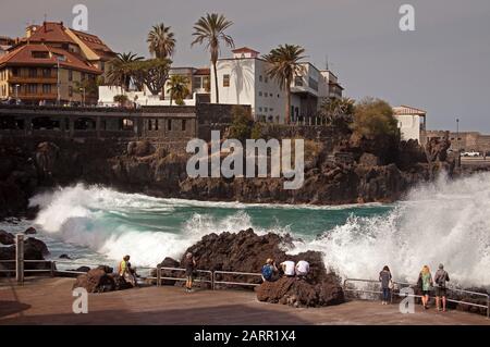 Kanarische Inseln, Puerto de a Cruz, Teneras. Januar 2020. Touristen kommen in die Nähe, um dramatische Wellen mit 23 Grad Celsius und duftigem Sonnenschein zu beobachten, der gegen die Felsen am San Telmo-Gehweg kragt. Stockfoto