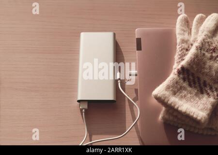 Kabelloses Aufladen des Laptops im Winter von der Powerbank ( Batterieladegerät ), auf rotem Hintergrund. Tragbares Ladegerät sehr produktiv, während B. Stockfoto