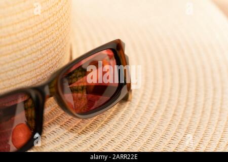 Sonneneinschätzung und Strohhut symbolisieren Ferien und Reisen in warme Länder. Tropische Früchte spiegeln sich in Sonnenschirmen wider. Farbbild mit Kopierbereich Stockfoto