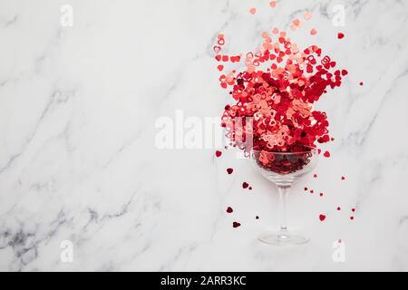 Champagnerglas überströmt mit rotem Valentinskerz Herzconfetti Stockfoto