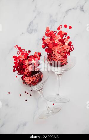 Champagnerglas überströmt mit rotem Valentinskerz Herzconfetti Stockfoto