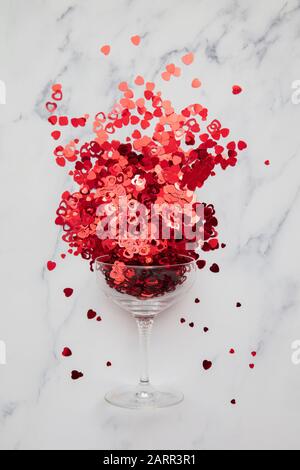 Champagnerglas überströmt mit rotem Valentinskerz Herzconfetti Stockfoto