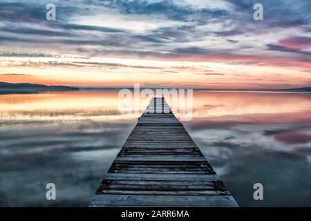 San Feliciano, Trasimeno-See, Perugia, Umbrien, Italien. Ein Holzsteg führt den Blick über den Sonnenuntergang zum Trasimeno-See mit einem schönen Sonnenuntergang. Stockfoto