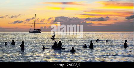 Silhouette einer Yacht und eine Gruppe von Touristen im ruhigen Wasser entlang des weißen Strandes von Boracay Island in farbenfrohem Sonnenuntergang, Philippinen Stockfoto