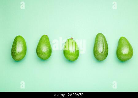 Frische reife organische grüne Avocados auf Farbhintergrund, Top-View-Konzept für Sommeressen. Minimaler flacher Lay Stil Avocado ganze Früchte auf Minzgrün Stockfoto