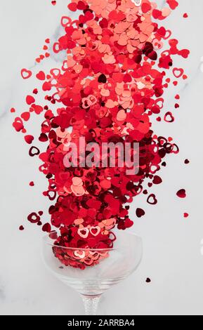 Champagnerglas überströmt mit rotem Valentinskerz Herzconfetti Stockfoto