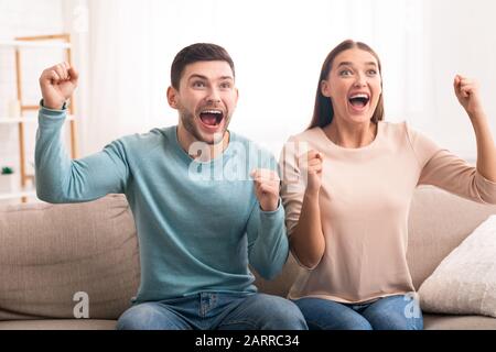 Aufgeregtes Paar, Das Sport Im Fernsehen Beobachtet Und Auf Sofa Sitzt Stockfoto