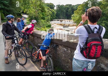 Touristen und Radfahrer halten an, um die Aysgarth Falls, Wensleydale, Yorkshire Dales National Park, England, zu betrachten Stockfoto