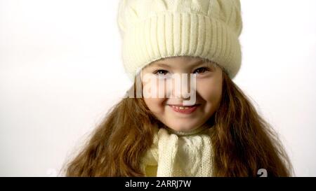 Porträt eines glücklichen Mädchens 5-6 Jahre alt. Kleines Mädchen mit langen Haaren in Strickmütze und Schal. Isoliert auf weißem Hintergrund. Stockfoto