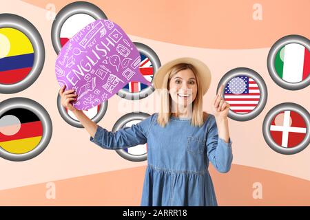 Schöne Frau mit Sprechblase und Flaggen verschiedener Länder auf Farbhintergrund. Studium der Fremdsprachen Stockfoto