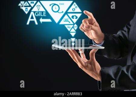 Geschäftsmann hält Tablet-PC mit digitalen Symbolen auf dunklem Hintergrund. Konzept der Geschäftsplanung Stockfoto