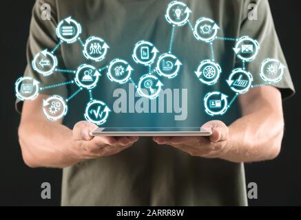 Geschäftsmann hält Tablet-PC mit digitalen Symbolen auf dunklem Hintergrund, Nahaufnahme. Konzept der Geschäftsplanung Stockfoto
