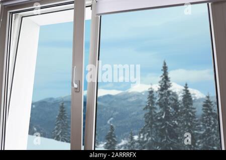 Blick auf den schönen verschneiten Wald durch ein großes Metall-Kunststoff-Fenster Stockfoto
