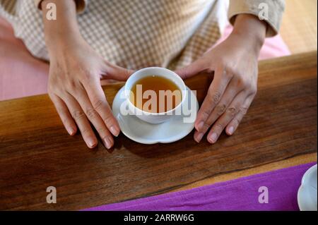 Weibliche Hände, die morgens einen heißen Tee auf Holztisch halten Stockfoto